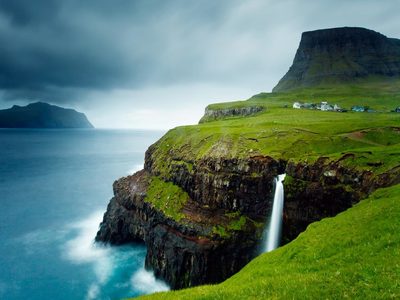 Village of Gásadalur below Heinanova mountain, with waterfall cascading over cliff into the Atlantic Ocean, Vágar, Faroe Islands (© Kimberley Coole/Lonely Planet)